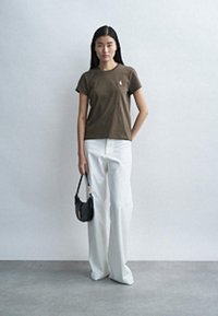 Brun t-skjorte med korte ermer og rund hals, kombinert med hvite bukser med vide ben og en liten svart håndveske. Glatt stoffstruktur.
