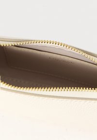 Valge tekstuuriga nahast kott kuldse tõmblukuga, millel on siledat siseosa ja kaarditasku. Avatud vaade, mis näitab detailset õmblustööd.