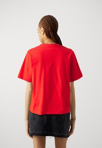 T-shirt en coton rouge à manches courtes et col rond, avec une coupe décontractée. Porté avec une jupe en denim noire à l'ourlet effiloché.