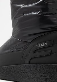 Černá zateplená bota vyrobená z hladkého materiálu, s texturovanou gumovou podrážkou a výrazným logem Bally na boku.