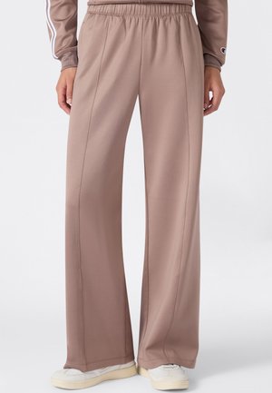 Pantalon beige à jambes larges avec taille élastique porté avec des baskets blanches et un haut à manches longues assorti sur un fond clair.