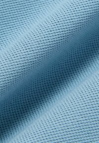 Light blue textured fabric with a fine waffle weave pattern, shown in soft folds.