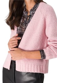 Rosafärgad stickad cardigan med ribbad nederkant och manschetter, med en avslappnad passform. Buren över en mönstrad blus med volangkrage.