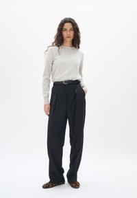 Maglione grigio chiaro a maniche lunghe, pantaloni neri a vita alta con pieghe, cintura nera con fibbia dorata e pantofole con stampa leopardata.