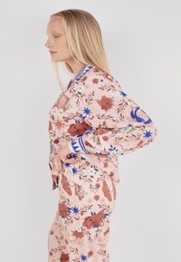 Bluse mit floralem Muster in Pink mit blauen und braunen Akzenten. Verfügt über einen Kragen, lange Ärmel und eine lockere Passform mit filigranen Designs.