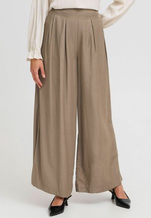 Beigeweite Hosen aus glattem Stoff mit vorderen Falten, hoher Taille und geradem Schnitt, kombiniert mit schwarzen spitzen Absätzen.