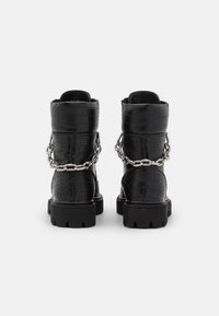 Botas de tobillo de cuero negro con textura de cocodrilo, detalle de cadena plateada y suela de goma gruesa. Cuenta con un cuello acolchado para mayor comodidad.