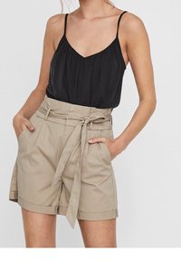 Top nero senza maniche con scollatura a V abbinato a pantaloni corta beige a vita alta con cintura e tasche laterali, realizzati in tessuto leggero.