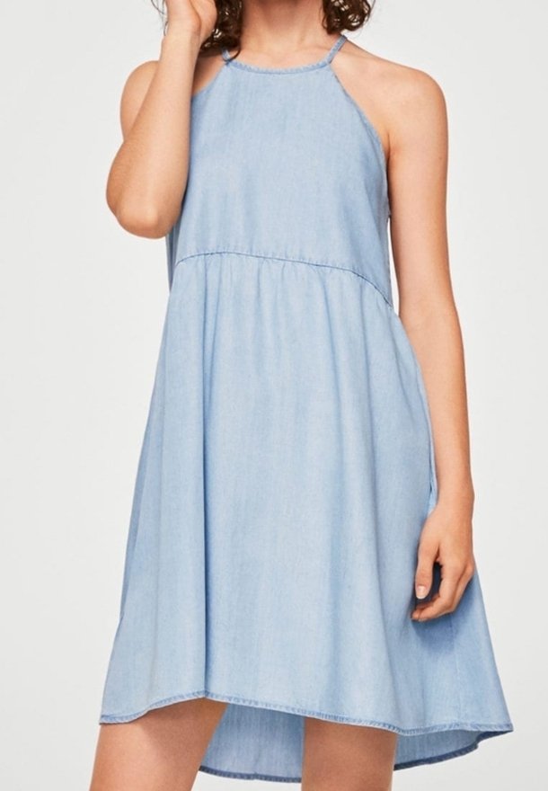 Femme portant une robe chambray bleu clair sans manches avec un col halter et une jupe légèrement évasée.