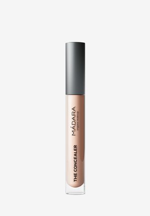Tube de correcteur de maquillage biologique Madara avec une teinte beige clair et un capuchon gris sur fond blanc.