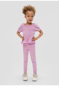 Rosa, kurzärmeliges Smocked-Oberteil mit floralem Muster und Peplum, kombiniert mit passenden floralen Leggings, getragen mit hellen Sneakers.