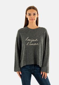 Grijze trui met lange mouwen en een ronde halslijn, met op de voorkant witte geborduurde tekst "bonjour l'amour". Zachte textuur.