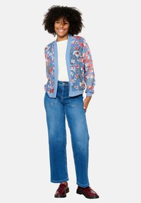 Ziedu bomber žakete zilā krāsā ar rozā un zaļiem rakstiem, kombinēta ar gaiši ziliem taisnām kājām džinsiem un tumši sarkaniem mokasīniem.