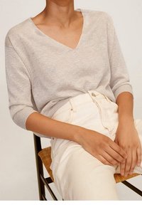 Light gray, V-neck sweater with three-quarter sleeves, soft texture. Paired with cream-colored high-waisted pants. Natural light setting.
