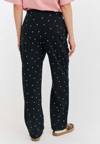 Čierne nohavice s bielymi bodkami, s elastickým pásom a voľným strihom, kombinované s hnedými topánkami s leopardo potlačou.