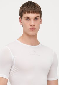 T-shirt de sport blanc à manches courtes avec un motif texturé, encolure ronde et logo de marque gris sur la poitrine. Design ajusté.