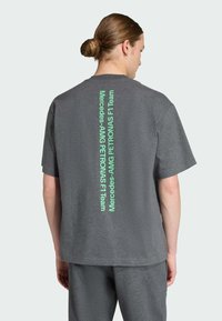 Camiseta de algodón gris con un logotipo de texto verde vertical en la parte posterior. Mangas cortas y un ajuste relajado, con un cuello redondo.