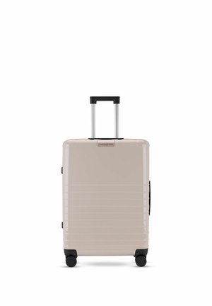 Beiger Hartschalenkoffer mit horizontalen Rillen, schwarzem ausziehbarem Griff und vier schwarzen Drehrollen.