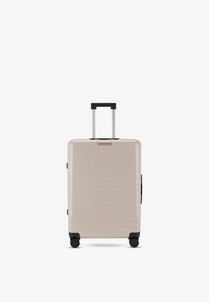 Beiger Hartschalenkoffer mit horizontalen Rillen, schwarzem ausziehbarem Griff und vier schwarzen Drehrollen.