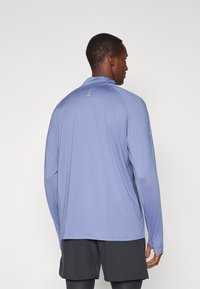Langsleeve sportshirt van licht paarse stof, met een hoge kraag en subtiele reflecterende accenten langs de achterkant en mouwen.