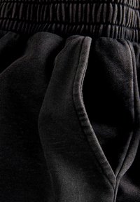 Schwarze Sweatpants mit einem elastischen Bund, die eine glatte Textur und runde Seitentaschen aufweisen. Sichtbare Nähte entlang der Nähte.