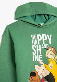 Groene hoodie met een zachte textuur, voorzien van een grafische print van een meisje en de tekst "WEES VROLIJK EN STRALEN" in het wit. Met capuchon.