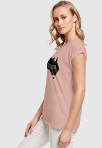 Lys rosa t-skjorte med korte oppbrettede ermer, med en svart kontur av Australia og ordet "AUSTRALIA" i fet tekst over brystet.