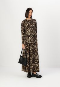 Kjole med leopardmønster og lange ermer, med en flytende silhuett og myk tekstur, kombinert med kraftige svarte sko og en liten svart håndveske.