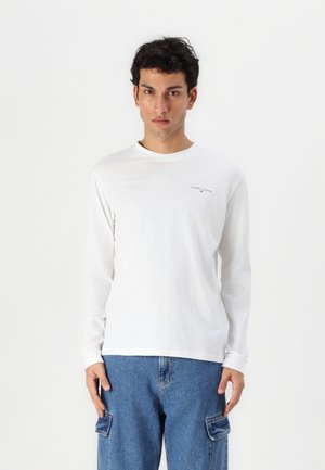 Vit långärmad t-shirt med rund halsringning och en liten "TOMMY JEANS"-logga på bröstet, kombinerad med blå cargo-jeans med sidofickor.