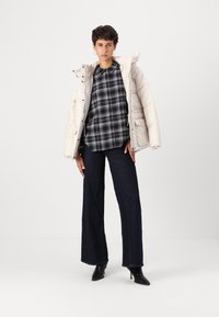 Puffer jacket in light beige, checked black and white shirt, dark wide-leg jeans, and black heeled boots. Smooth textures, structured design.