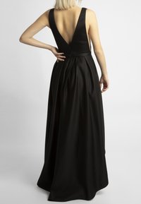 Schwarzes Abendkleid mit tiefem V-Ausschnitt am Rücken, breiten Trägern und bodenlanger, plissierter Sch skirt. Hergestellt aus glattem, satinähnlichem Material.