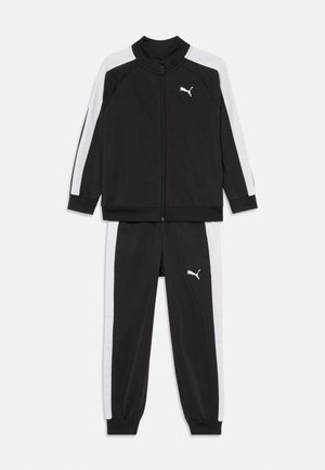 Compleu sportiv negru cu dungi albe pe laterale, formând un sacou cu fermoar și pantaloni asortati. Confectionat dintr-un material neted și ușor.