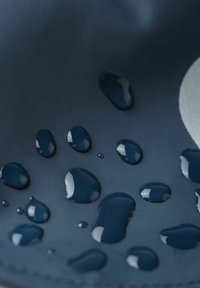 Marines wasserfestes Material mit Wassertropfen auf der Oberfläche. Hat eine glatte Textur und einen dezenten Glanz, mit kontrastierenden, glänzenden Akzenten.