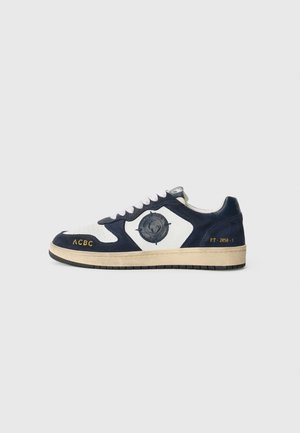 Sneakers blu e bianchi in materiale scamosciato e in pelle, con un'emblema rotonda, suole testurizzate e dettagli stampati in oro sul lato.