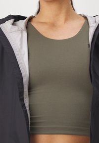 Top corto ajustado de color verde oliva hecho de tela suave, combinado con una chaqueta negra con cierre de cremallera que presenta un forro interior gris claro.