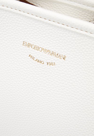 Hvid læder med en tekstureret finish, der har et guldpræget logo: "EMPORIO ARMANI MILANO 1981" nær toppen.