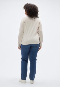 Beige long-sleeve top with a smooth texture, paired with dark blue jeans. The top has a rounded hem and the jeans are straight-cut.