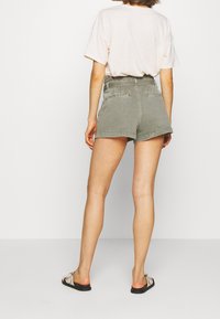 Shorts de mezclilla verde caqui con cintura alta, dobladillo enrollado y dos bolsillos traseros, combinados con una camiseta holgada de color rosa claro.