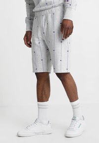 Grijze jersey shorts met paarse verticale strepen en kleine logoaccenten, voorzien van een elastische tailleband en een ontspannen pasvorm. gedragen met witte sneakers.