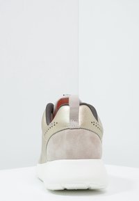 Sneaker featuring a combination of light beige suede and metallic gold accents, with a textured back, padded collar, and white sole.