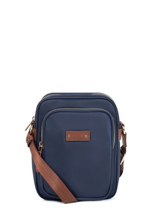 Sac bandoulière compact bleu marine avec sangle marron réglable, poche avant zippée et écusson en cuir de la marque sur fond blanc.