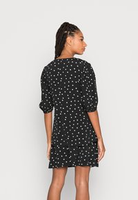 Vestido preto com bolinhas, mangas bufantes, barra com volantes e ajuste solto. Feito de um tecido leve, apresenta um decote redondo e linhas limpas.