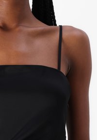 Top de satén negro con tirantes finos, una textura suave y un diseño sencillo con escote recto. Sin patrones visibles ni herrajes.