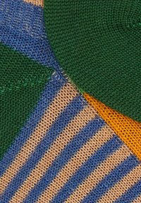 Primo piano di un tessuto lavorato a maglia con motivi a righe verdi, blu e beige, e un piccolo tratto di arancione.