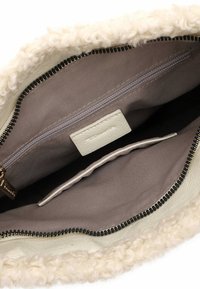 Intérieur de sac à main en fourrure blanche et crème avec une poche zippée, doublure beige et un patch avec une étiquette. Comprend un détail de fermeture éclair noir contrastant.