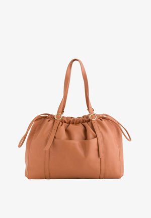 Sac à main en cuir souple couleur beige clair avec haut froncé, deux bretelles avec anneaux dorés et une poche avant plate sur fond blanc.