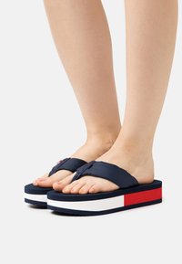 Navy blue flip-flops with fabric straps, a thick white and red-accented platform sole, and a textured footbed. Suitable for casual wear.