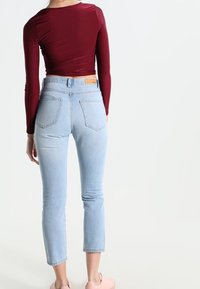 Burgundy dlouhý rukáv crop top spárovaný se světle modrými džíny s vysokým pasem a klasickým pětikapsovým designem. Měkká textilie.