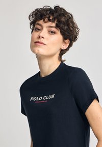 Schwarzes Baumwoll-T-Shirt mit Rundhalsausschnitt und kurzen Ärmeln, mit in Weiß und Rot bedrucktem Text "POLO CLUB" und "ESTABLISHED 2012".