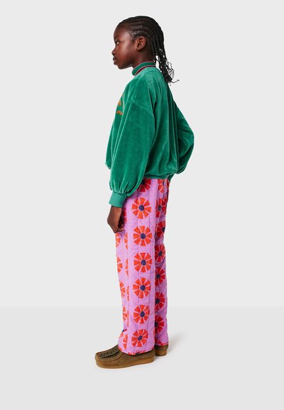 Grüner Samt-Sweatshirt mit rundem Kragen, gesteppte rosa Hose mit roten Blumenmustern und braunen Plateauschuhen.